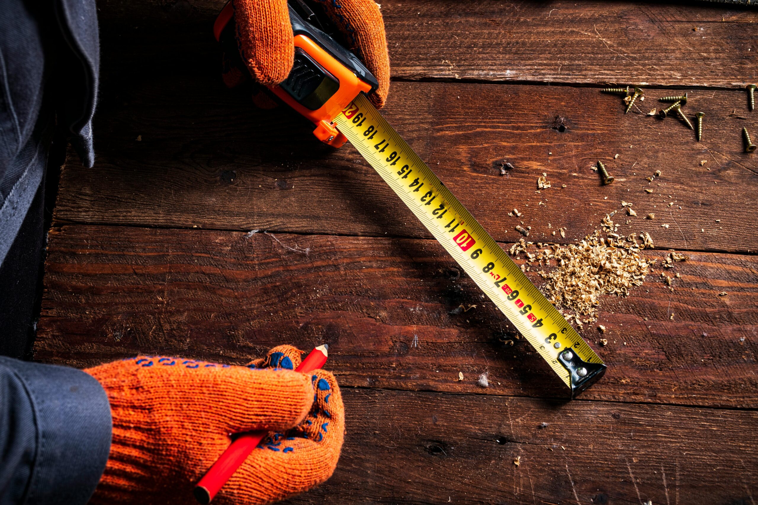 Close-up of gloved hands using a tape measure on wooden surface for precise carpentry.